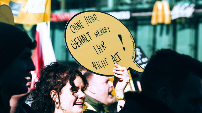 Eine lächelnde Demonstriende hebt am verdi Jugendstreiktag der Tarifrunde öffentlicher Dienst Bund und Kommunen in Hannover 2023 ein Schild hoch auf dem steht: ohne mehr Gehalt werdet ihr nicht alt! ein Schild hoch auf dem steht