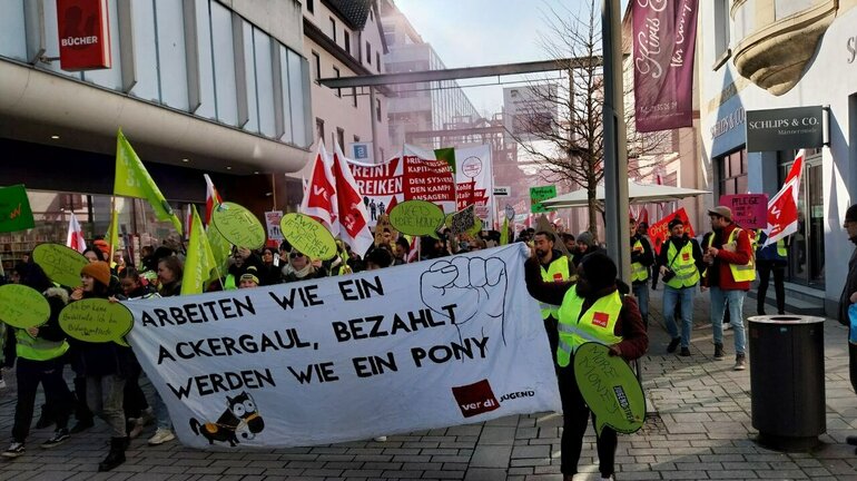 Am verdi Jugendstreiktag der Tarifrunde öffentlicher Dienst Bund und Kommunen 2023 in Esslingen ziehen Demonstrierende mit gelben verdi Westen, Fahnen und Schildern die Straße lang. In erster Reihe halten sie ein Banner auf dem steht: arbeiten wie ein Ackergaul, bezahlt werden wie ein Pony