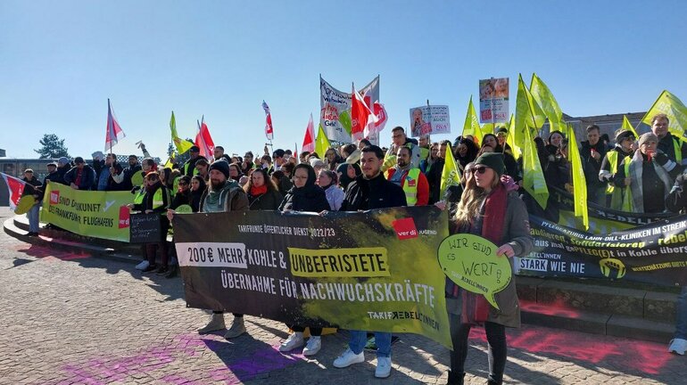 Demonstrierende Menschenmenge versammelt sich mit Fahnen und Schildern ausgestattet am verdi Jugendstreiktag der Tarifrunde öffentlicher Dienst Bund und Kommunen 2023 in Kassel. Die erste Reihe hält ein Banner auf dem steht 200 Euro mehr Kohle und unbefristete Übernahme für Nachwuchskräfte