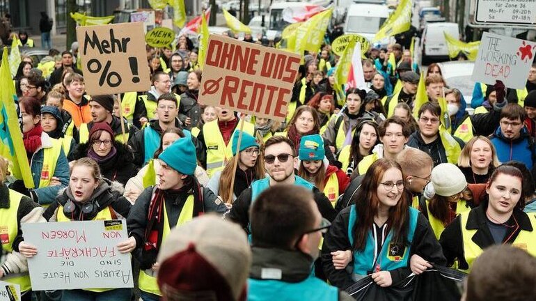 eine große Gruppe Streikende in ver.di Jugend Streikwesten in blau und grün.