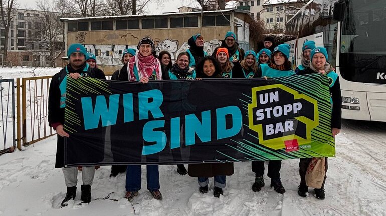 Eine Grupe Jugendlicher mit blauen Mützen mit dem Unstoppbar-Logo hält ein Banner, auf dem "Wir sind Unstoppbar" steht.