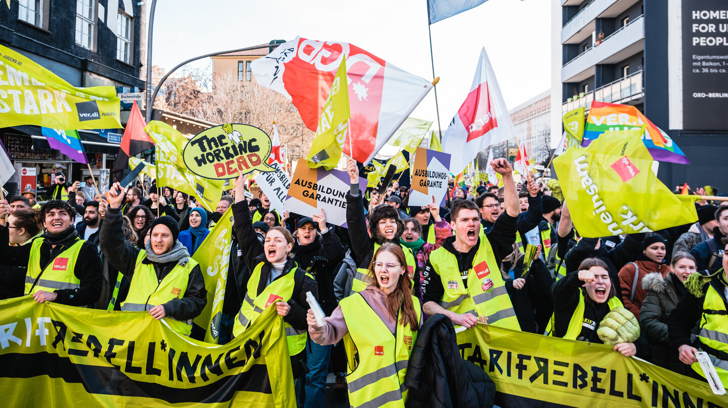 Große Gruppe Demonstrierender läuft lautstark mit gelben verdi Westen, diversen Fahnen, Schildern und Tarifrebellinnen Banner in Richtung Kamera. Anlass ist der verdi Jugendstreiktag der Tarifrunde öffentlicher Dienst Bund und Kommunen in Berlin 2023